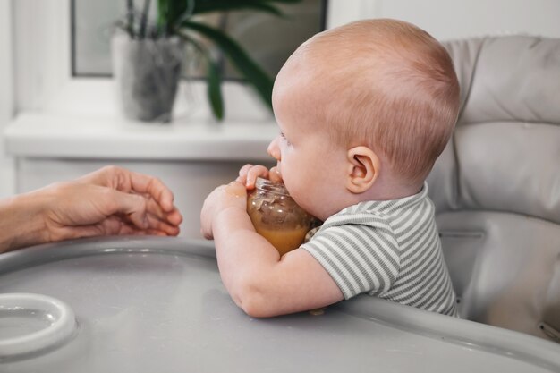 Mutter füttert Baby rein vom Löffel im Hochstuhl zu Hause