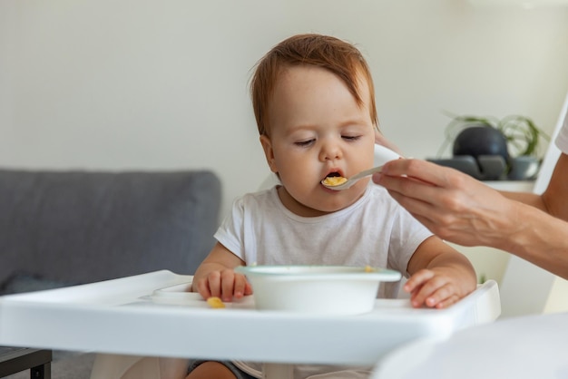 Mutter füttert ein kleines Kind, das zu Hause am Tisch der Kinder sitzt