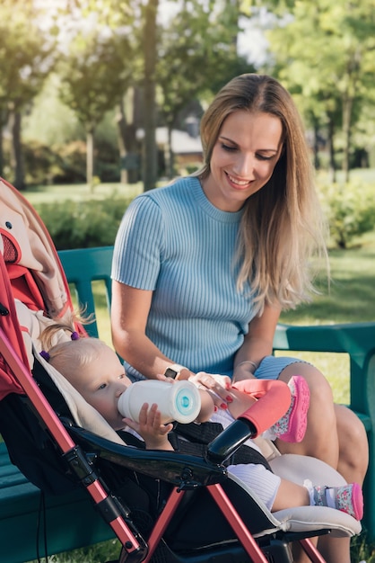 Mutter füttert hungriges Baby aus der Flasche im Wagen im Freien. Formel für die Ernährung von Kindern