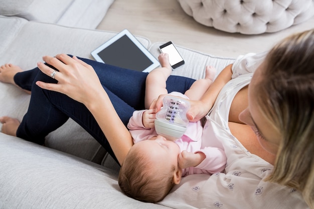 Mutter füttert ihr Baby mit Milchflasche im Wohnzimmer