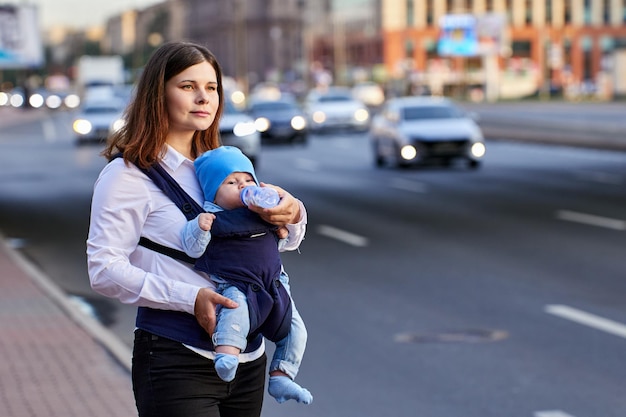 Mutter gibt Baby im Tragetuch, um Wasser aus der Flasche im Freien zu trinken