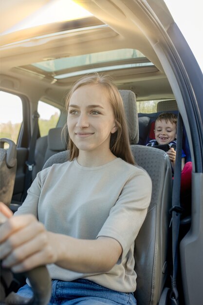 Mutter gibt dem telefon einen kleinen jungen, der auf einem autositz sitzt. sicherheit beim transport von kindern