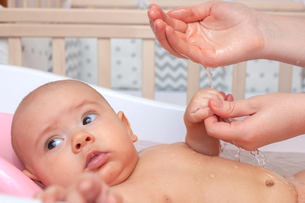 Mutter gießt Wasser aus ihrer Handfläche auf das Baby im Badezimmer. Selektiver Fokus