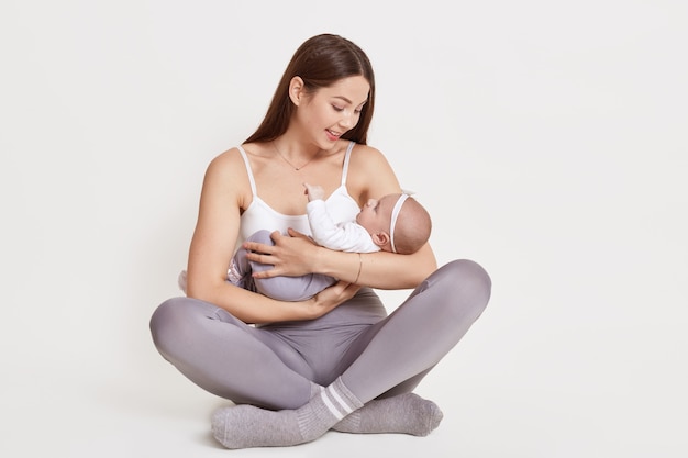 Mutter hält neugeborenes Baby beim Sitzen auf dem Boden mit gekreuzten Beinen