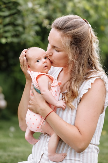 Mutter hält und küsst ihr Baby im Freien am Sommertag.