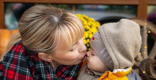 Mutter hat Spaß mit ihrem kleinen Sohn im Freien im Herbstpark. Mama küsst ihr kleines Baby, Nahaufnahme. Liebe und Fürsorge. Herbst- und Erntedankfest-Partyhintergrund.