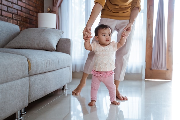 Mutter hilft ihrem Baby, ihre ersten Schritte zu Hause zu gehen