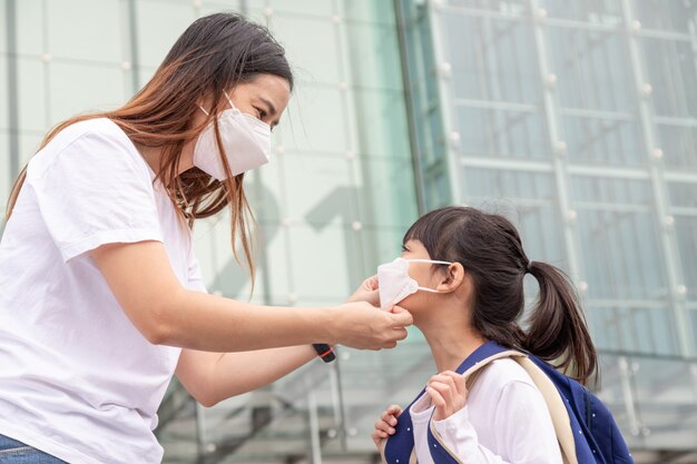 Mutter hilft ihrer Tochter beim Tragen einer medizinischen Maske zum Schutz des Ausbruchs von Covid19