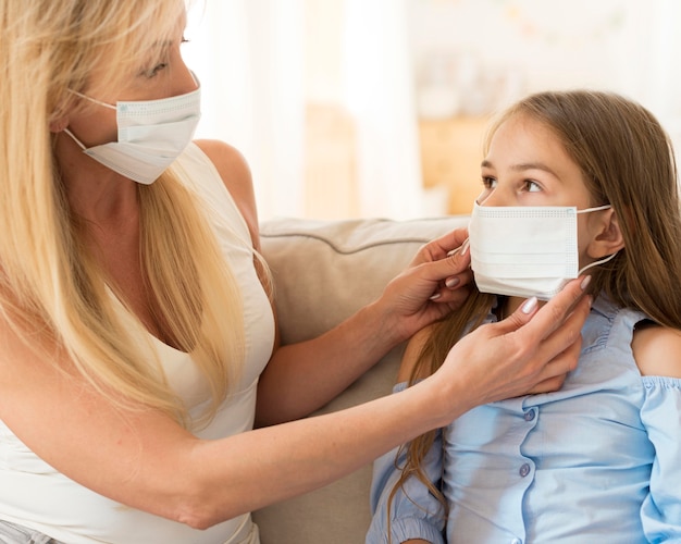 Foto mutter hilft tochter, medizinische maske auf ihr gesicht aufzusetzen