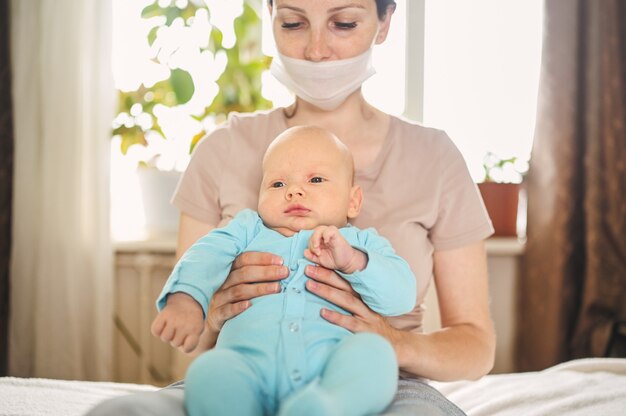 Mutter in schützender Gesichtsmaske, die ihren neugeborenen Sohn hält