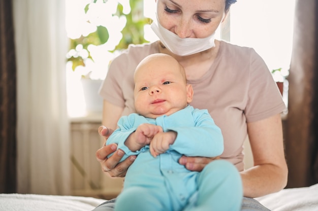 Mutter in schützender Gesichtsmaske, die ihren neugeborenen Sohn hält