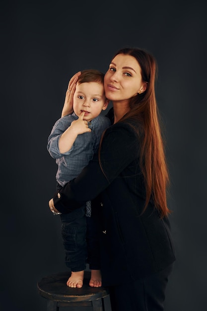 Mutter in stylischer schwarzer Kleidung ist mit ihrem kleinen Sohn im Studio