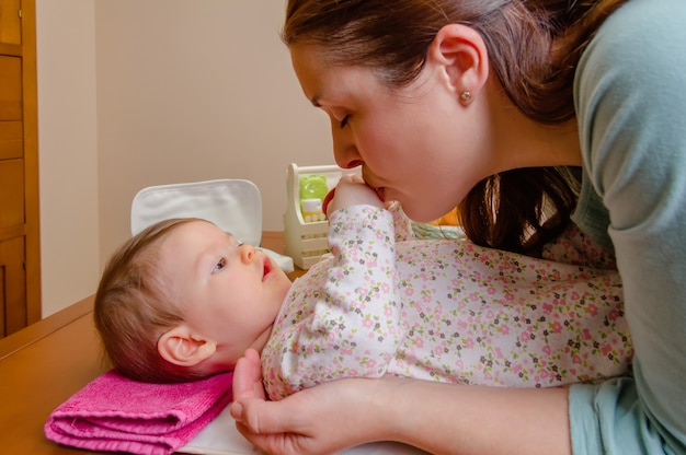 Mutter küsst die Hände ihres Babys, das nach dem Windelwechsel liegt