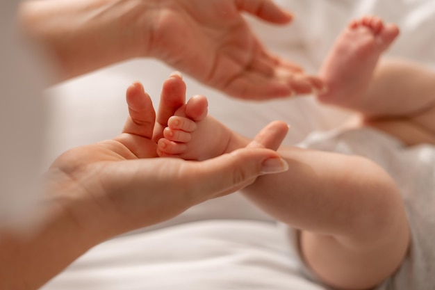 Mutter küsst die nackten Füße des Babys, hält sie in ihren Händen und massiert seine Füße, gesundes, aktives Kind