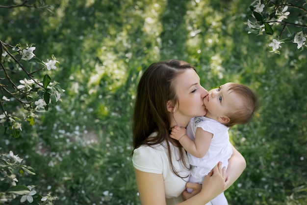 Mutter küsst ihre kleine Tochter in einem blühenden Apfelgarten