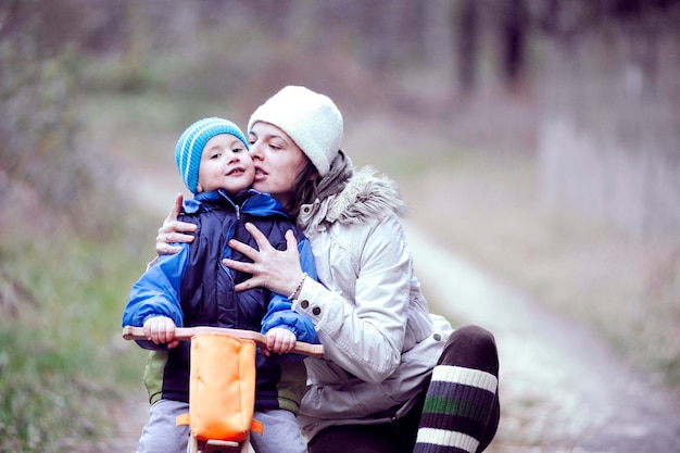Mutter küsst ihren Sohn, der im Winter im Park Fahrrad fährt