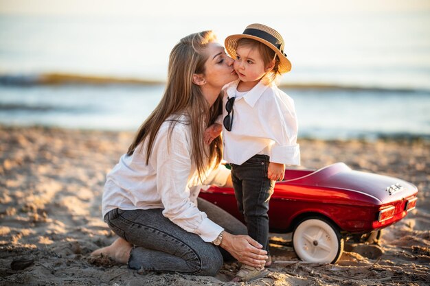 Mutter küsst zärtlich ihre kleine Tochter in einem Hut und amüsiert sich zusammen am Strand des Ostsees als glückliche Familie