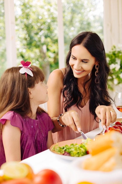 Mutter lächelt, während sie Salat für ihre Tochter gibt