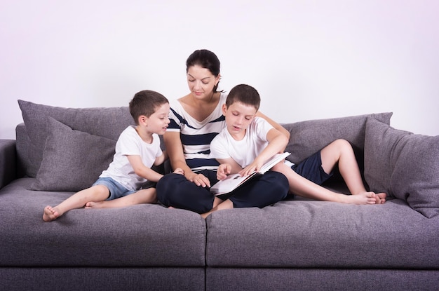 Mutter liest ein interessantes Buch mit ihren Söhnen auf dem Sofa Studioportrait auf weißem Hintergrund