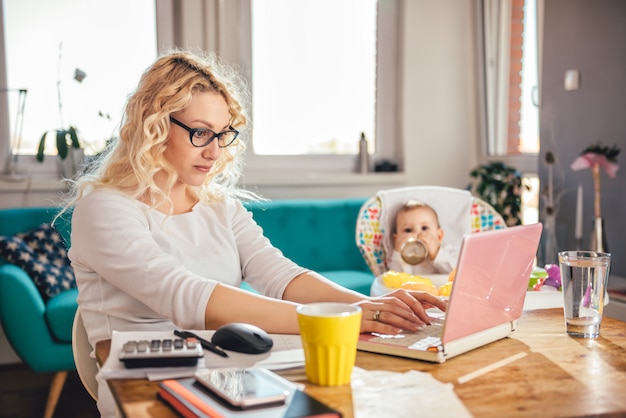 Foto mutter mit dem baby, das zu hause büro des laptops verwendet