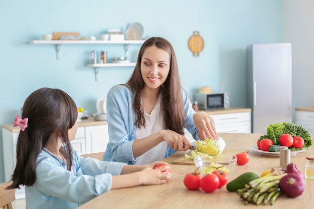 Mutter mit der niedlichen Tochter, die Gemüsesalat in der Küche vorbereitet