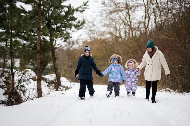 Mutter mit drei Kindern, die Händchen halten und im Winterwald spazieren gehen