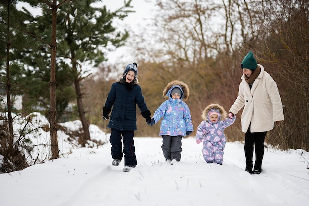 Mutter mit drei Kindern, die Händchen halten und im Winterwald spazieren gehen