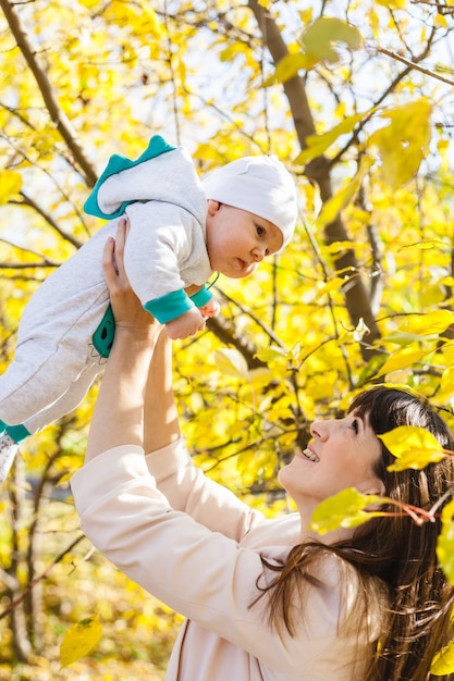 Mutter mit einem Baby, ein kleiner Junge geht im Herbst in den Park oder Wald. Gelbe Blätter, die Schönheit der Natur. Kommunikation zwischen einem Kind und einem Elternteil.