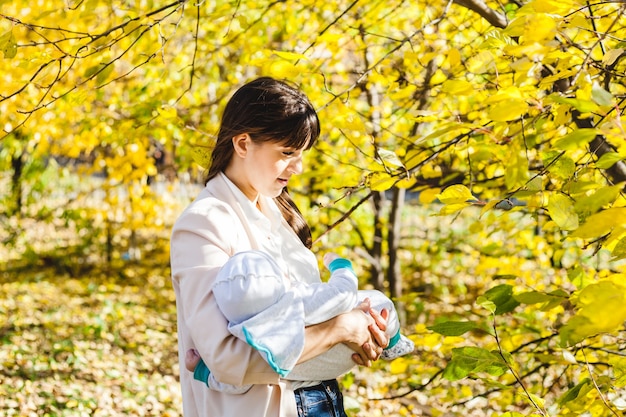 Mutter mit einem Baby, ein kleiner Junge geht im Herbst in den Park oder Wald. Gelbe Blätter, die Schönheit der Natur. Kommunikation zwischen einem Kind und einem Elternteil.