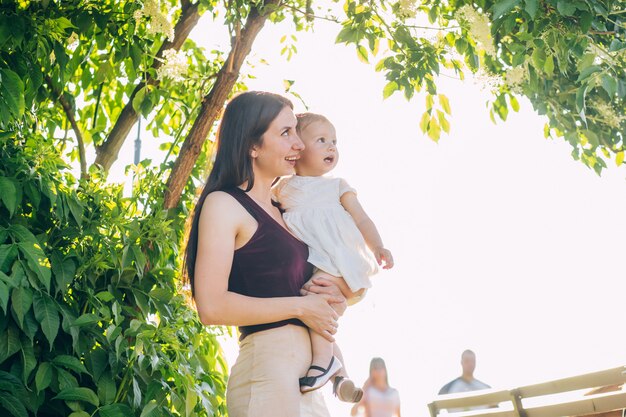 Mutter mit einem Baby in den Armen an einem sonnigen Tag geht durch den Park.