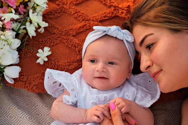 Mutter mit einem neugeborenen Baby liegt am Strand, weiße Kleider, Blumen liegen in der Nähe