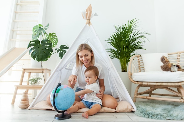 Mutter mit einer kleinen Tochter sitzt zu Hause in einem Wigwam und studiert den Globus.