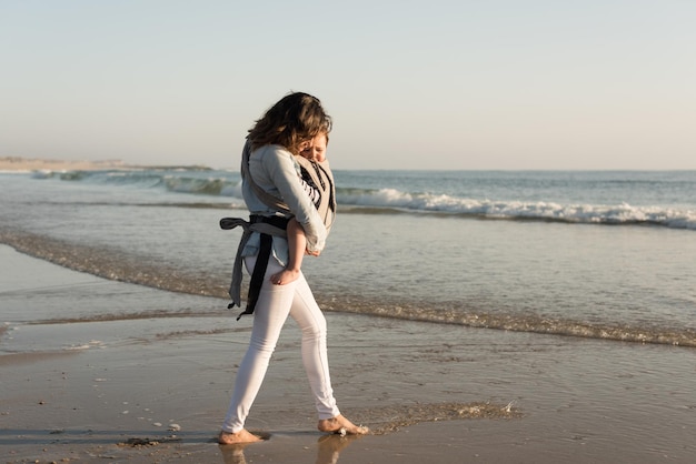 Mutter mit Ergobaby mit Kleinkind am Strand