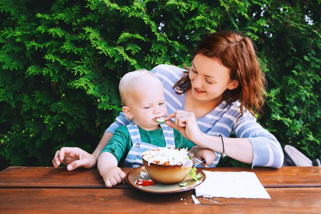 Mutter mit ihrem Kind isst zusammen und hat Spaß im Restaurant im Park auf Naturhintergrund