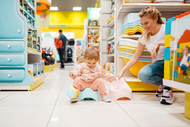 Mutter mit ihrem kleinen Mädchen, das Babytöpfchen im Kindergeschäft wählt.