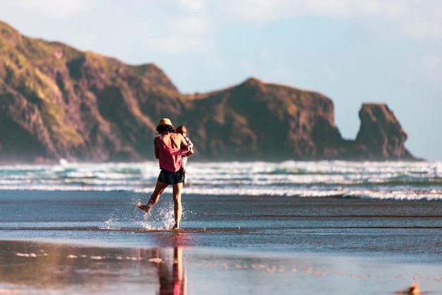 Mutter mit ihrem Sohn, der Wasser an der Küste in Neuseeland spritzt.