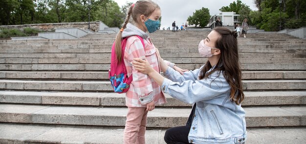 Mutter mit ihrer kleinen Tochter, einem Schulmädchen, vor dem Hintergrund der Schritte auf dem Weg zur Schule. Coronavirus-Pandemie-Bildungskonzept.