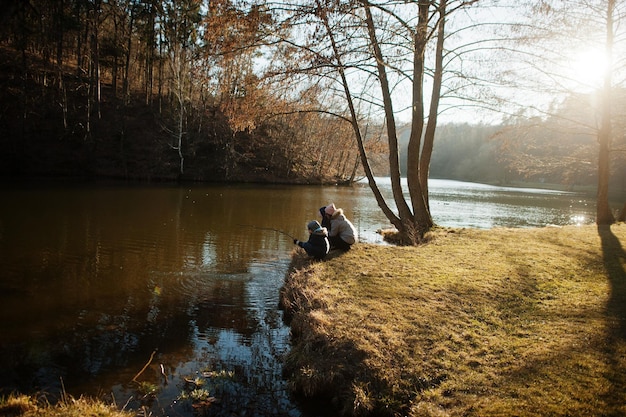 Mutter mit Kindern, die im Vorfrühlingspark mit einem Stock im Pfund fischen