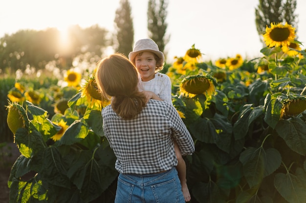 Mutter mit kleinem Sohn im Sonnenblumenfeld während der goldenen Stunde Mutter und Sohn sind in der Natur aktiv