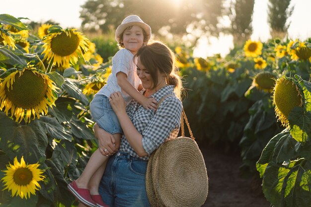 Mutter mit kleinem Sohn im Sonnenblumenfeld während der goldenen Stunde Mutter und Sohn sind in der Natur aktiv
