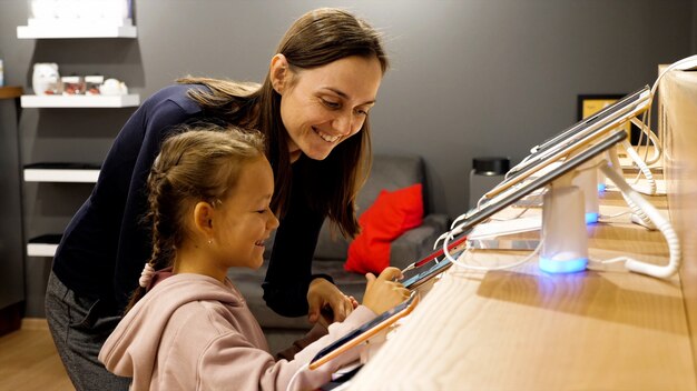 Foto mutter mit kleiner tochter, die ein neues smartphone in einem elektronikgeschäft wählt.