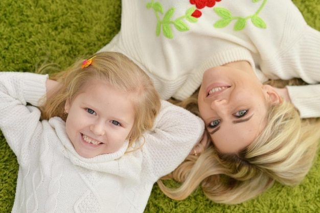 Mutter mit kleiner Tochter, die zu Hause auf grünem Teppich liegt