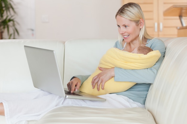 Mutter mit Laptop auf der Couch, die ihr Baby hält