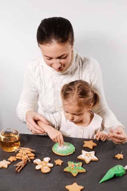 Mutter mit Mädchen schmückt Lebkuchen zu Weihnachten