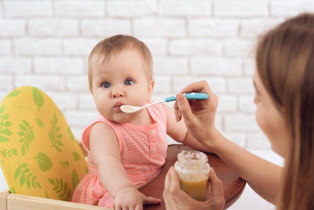 Mutter mit Püree und Löffel füttert kleines Baby