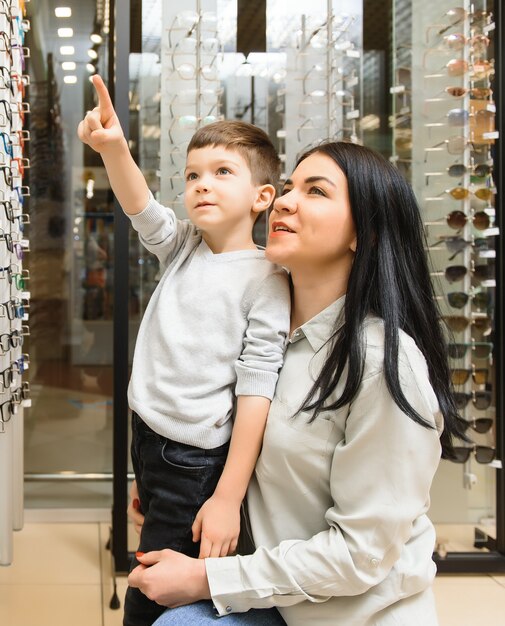 Mutter mit Sohn, der eine Brille im Optikgeschäft wählt.