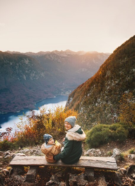 Mutter mit Sohn wandern und ruhen auf Holzbank im Alpenherbst am Bohinjer See Slowenien