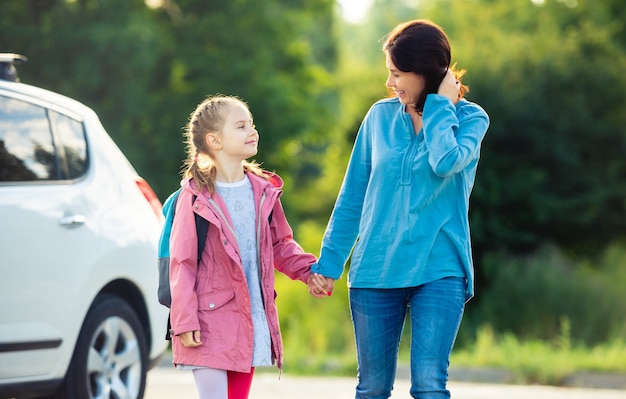 Mutter mit Tochter, die auf dem Parkplatz im Freien Händchen haltend zur Schule zurückgeht