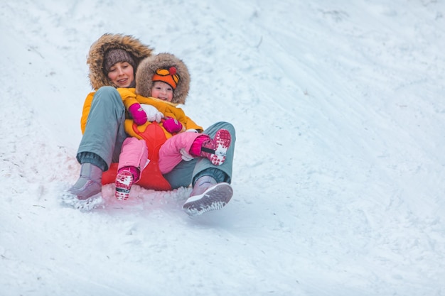 Mutter mit Tochter, die vom Winterhügel schiebt