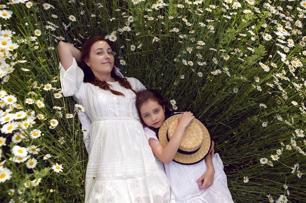 Mutter mit Tochter in einem weißen Kleid liegen auf einem Kamillenfeld